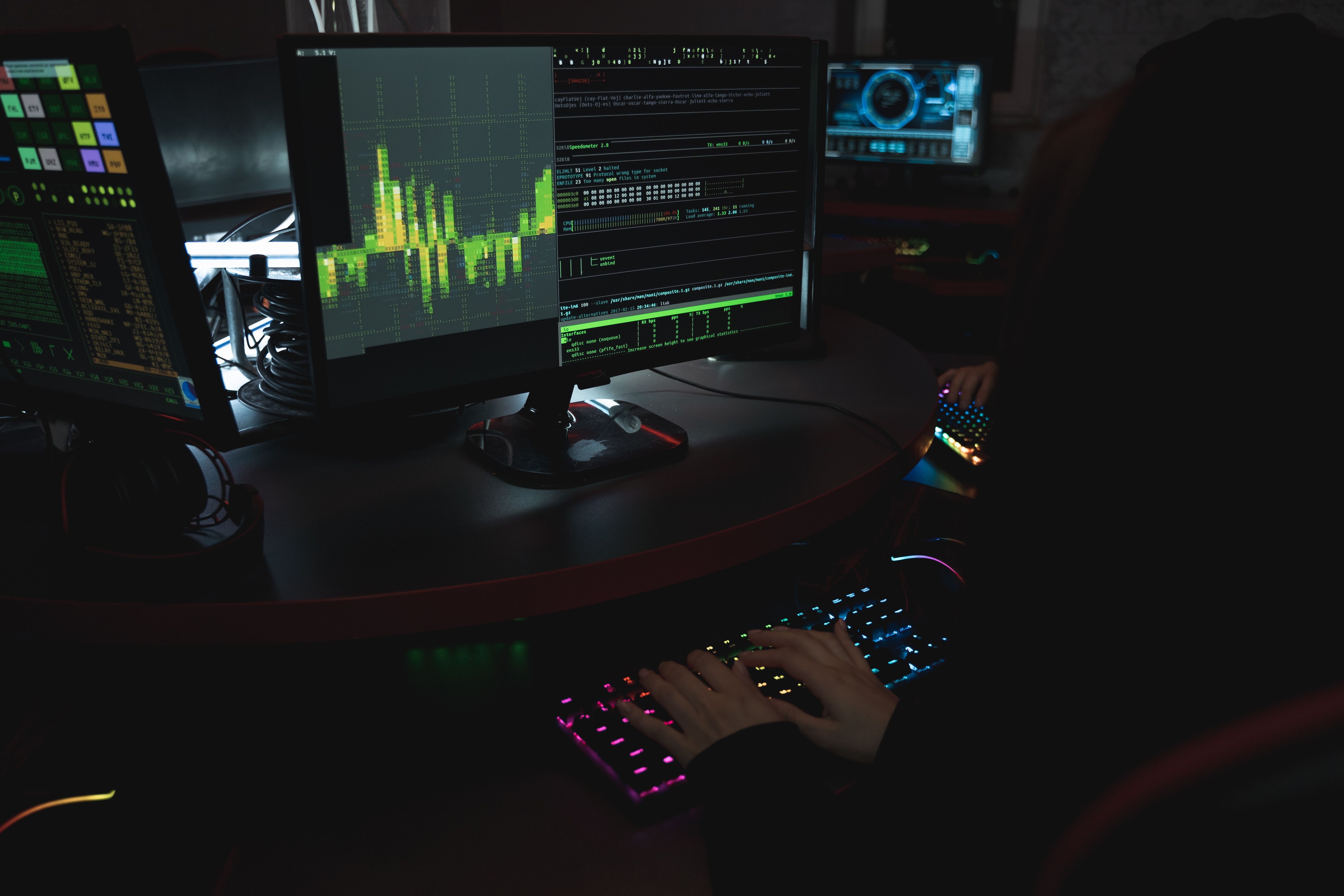 Cybersecurity professional working across multiple monitors in a dark workspace